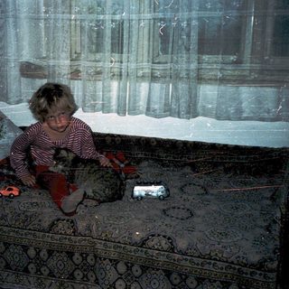 Child sitting on bed in dimly lit room.