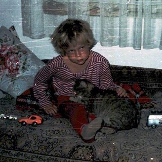 Child sitting on bed in dimly lit room.