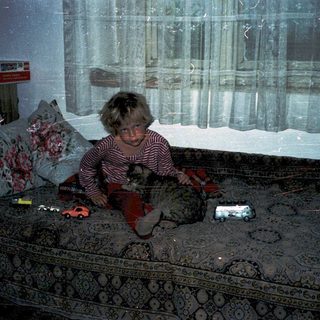 Child sitting on bed in dimly lit room.