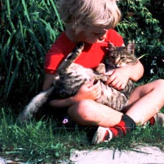 Child hugging cat outdoors on grass.
