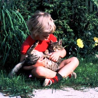 Child hugging cat outdoors on grass.