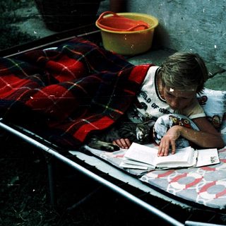 Child reading outdoors on a blanket.
