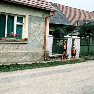 Two children standing near a rustic house.