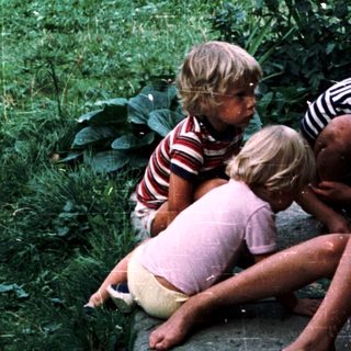 Four children sitting together outdoors near water.