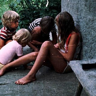 Four children sitting together outdoors near water.