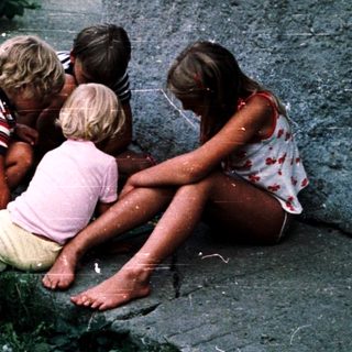 Four children sitting closely outdoors near plants.