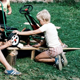 Three children playing with toy cars on grass.