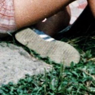 Three children playing with toy cars on grass.