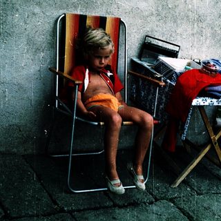Child sitting alone on folding chair outdoors.