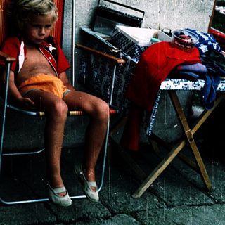 Child sitting alone on folding chair outdoors.