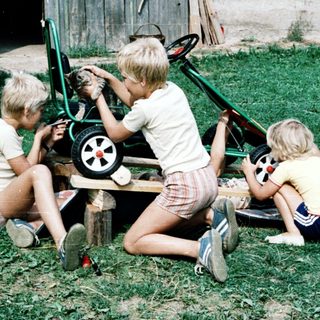 Three children repairing a toy wagon outdoors.
