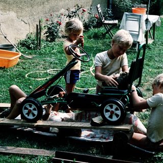 Three children playing with homemade toy cart.