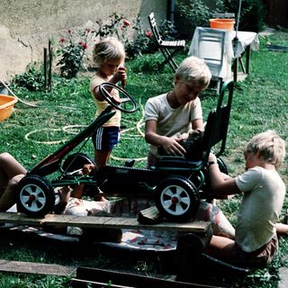 Three children playing with homemade toy cart.
