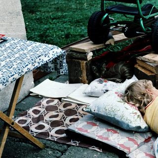 Child resting on grass near toy lawn mower.