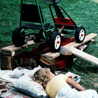 Child resting on grass near toy lawn mower.