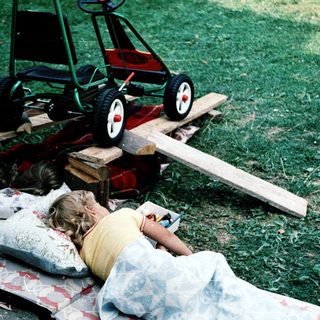 Child resting on grass near toy lawn mower.