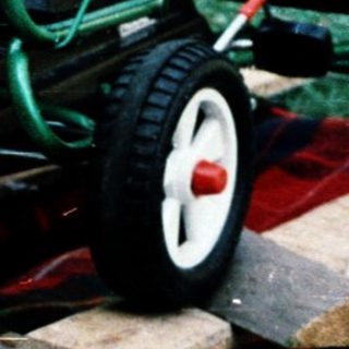 Child resting on grass near toy lawn mower.