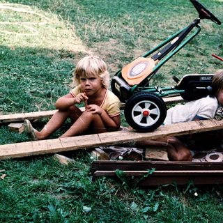 Two children playing with toy lawn mowers.
