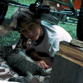 Child petting cat in grassy outdoor area.
