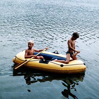 Two people rowing on an inflatable boat in water.