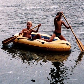Two people rowing inflatable boat on calm lake.
