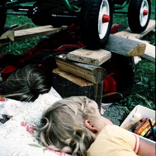 Child resting on picnic blanket outdoors with cat nearby.