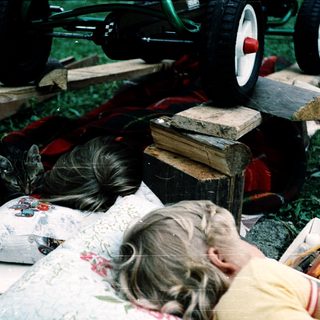 Child resting on picnic blanket outdoors with cat nearby.