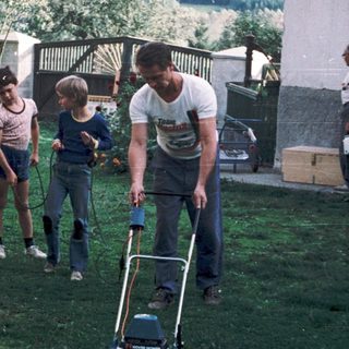Family mowing lawn with children and dog nearby.