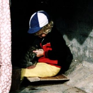 Child sitting under makeshift shelter, another child observing.