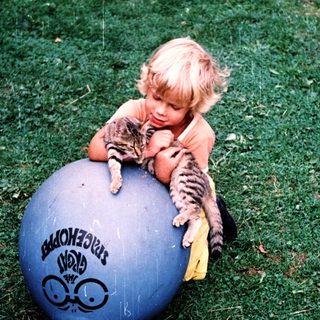 A child plays with a cat on a blue exercise ball.