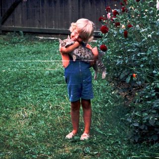 Child smelling roses in a garden.