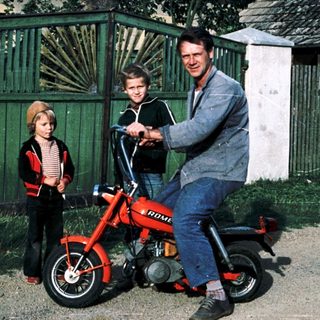 Family posing with vintage red motorcycle.