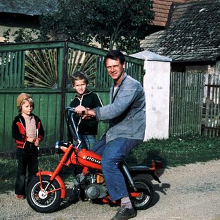 Family posing with vintage red motorcycle.