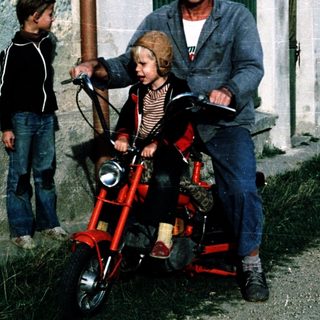 Family enjoying outdoor ride on red motorcycle with child seats.