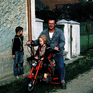 Family enjoying outdoor ride on red motorcycle with child seats.