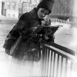 Person reading book outdoors near historic building.