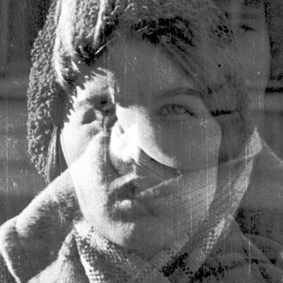 Blurred black-and-white portrait of a person scratching their neck.