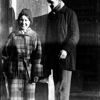 Two people posing outside an institution in winter attire.