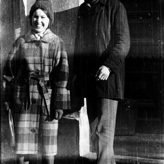 Two people posing outside an institution in winter attire.
