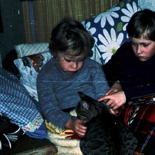 Two children playing with a cat indoors.