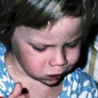 Child eating cereal in bed with book nearby.