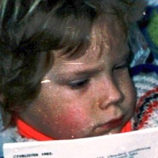Child reading comic book with curious cat nearby.