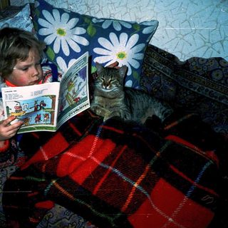 Child reading comic book with curious cat nearby.