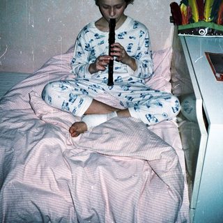 Child playing recorder in pajamas on a bed.