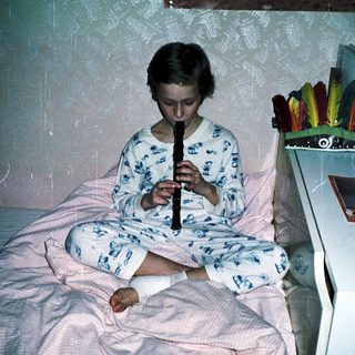 Child playing recorder in pajamas on a bed.