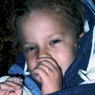 Child wrapped in blanket, looking up curiously.