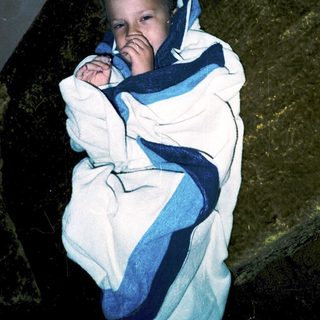 Child wrapped in blanket, looking up curiously.