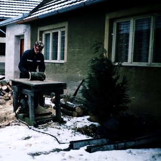 Man operating woodworking machine in snowy backyard.