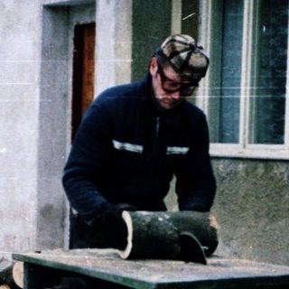 Man operating woodworking machine in snowy backyard.