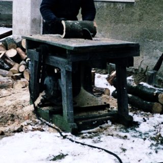 Man operating woodworking machine in snowy backyard.